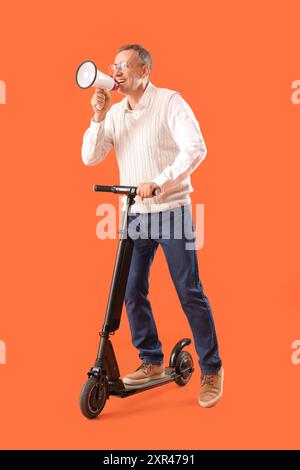 Reifer Geschäftsmann in Brille mit Elektroroller, der in Megaphon auf orangem Hintergrund schreit Stockfoto