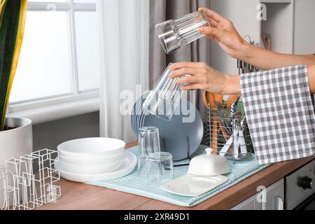 Weibliche Hände halten saubere Gläser in der Nähe von Geschirr auf der Theke in der Küche Stockfoto