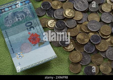 Terengganu, Malaysia - 24. August 2024 : Nahaufnahme der verstreuten malaysischen Münzen und 50 Ringgit malaysisches Geld auf grünem Hintergrund Stockfoto