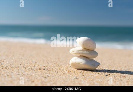 Weiße Steine stapelten sich auf dem Sandstrand mit dem blauen Meer im Hintergrund. Stockfoto
