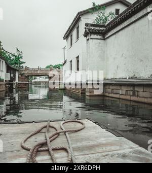 Ein Blick von einem Holzboot, das einen schmalen Kanal in Suzhou, China, hinunterfährt. Der Kanal ist gesäumt von traditionellen weißen Häusern und eine Steinbrücke kann s sein Stockfoto