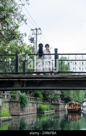 Suzhou, China - 11. Juni 2024 : zwei Frauen in traditioneller chinesischer Kleidung stehen auf einer Brücke mit Blick auf einen Kanal. Stockfoto