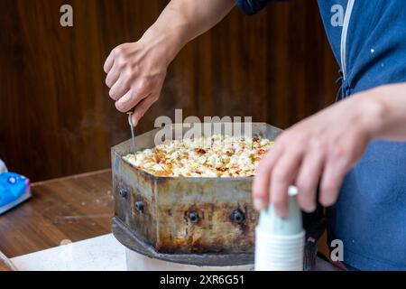 Suzhou, China - 11. Juni 2024 : Eine Person bereitet Essen in einer Metallpfanne auf einem Holztisch zu. Stockfoto