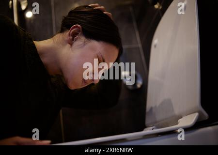 Bad, Erbrochenes und Frau mit Übelkeit, Boden und Symptomen von Lebensmittelvergiftung, Schmerzen und müde von Krankheit. Haus, Toilette und Kopfschmerzen von Menschen auf dem Boden Stockfoto