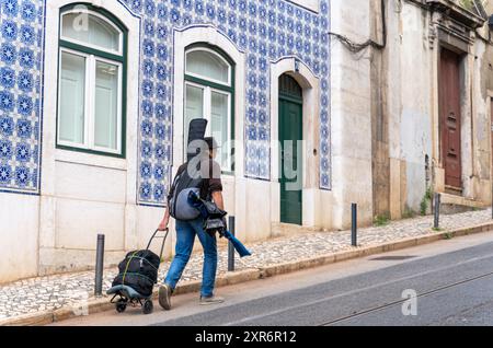 Ein Musiker mit Gitarre auf dem Rücken, der durch die Straßen von Lissabon, Portugal, spaziert Stockfoto