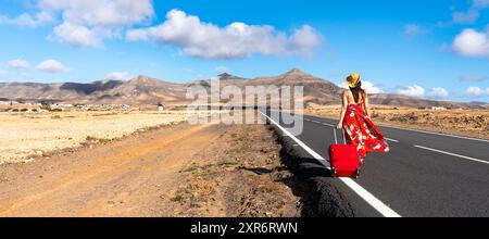 Frau mit rotem Koffer auf einer verlassenen Straße in der trockenen Landschaft Stockfoto