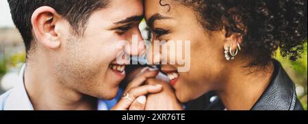 Nahaufnahme eines jungen interrassischen Paares, das draußen einen intimen Moment teilt. Ihre fröhlichen Ausdrücke und körperliche Nähe vermitteln tiefe Zuneigung und Stockfoto
