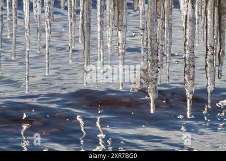 Heute ist ein sonniger Frühlingstag. Viele transparente Eiszapfen hängen über dem rastlosen blauen Wasser. Zahlreiche Tropfen fallen von ihnen. Das Sonnenlicht reflektiert sich auf t Stockfoto
