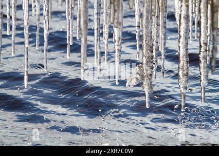 Es ist ein sonniger Frühlingstag. Viele Eiszapfen hängen über dem abgehackten blauen Wasser. Zahlreiche Tropfen fallen von ihnen. Stockfoto