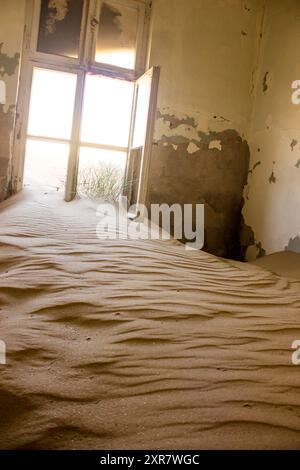 Sand fließt durch ein offenes Fenster in einen Raum in der halb begrabenen Geisterstadt Kolmanskuppe in Namibia. Stockfoto