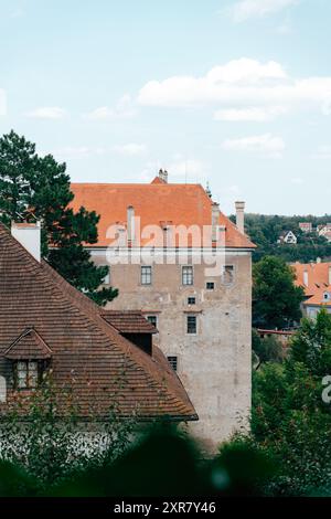 Ein bezaubernder Blick auf ein historisches Gebäude mit markanten orangen Dächern liegt eingebettet zwischen üppigem Grün unter einem hellblauen Himmel. Der friedliche geldautomat Stockfoto