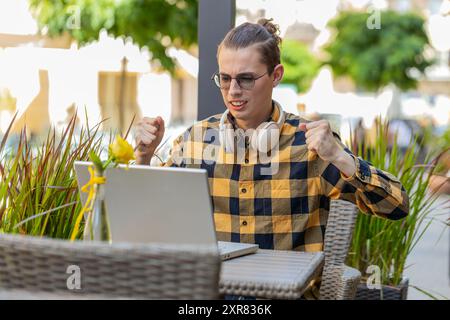 Gutaussehender junger Mann, der Laptop-Computer benutzt, um zu surfen, verliert überraschte plötzliche Lotterieergebnisse, schlechte Nachrichten, Verlust von Vermögen, scheitern. Guy sitzt draußen auf der Terrasse des städtischen Cafés. Lebensstil in der Stadt. Stockfoto