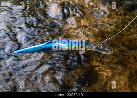 Der blaue Wobbler schwimmt auf der abgehackten Oberfläche des Wassers über dem flachen Wasser des Flusses. Sonnenflecken sind auf dem Kiesboden sichtbar. Stockfoto