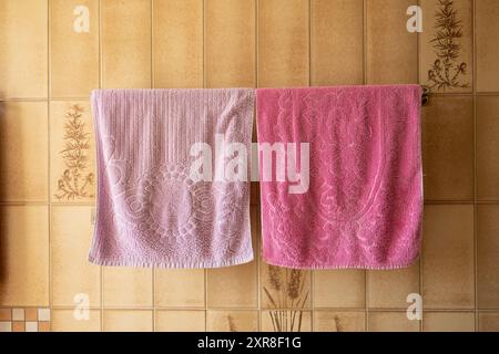 Frische Handtücher in hellen Farben hängen an einem Metallbügel im Badezimmer, der an der Wand mit Vintage-Fliesen befestigt ist. Stockfoto