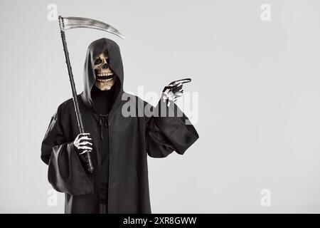 Mann im Halloween-Sensenmann-Todeskostüm, der Zeigefinger zur Seite auf Studiohintergrund zeigt. Stockfoto