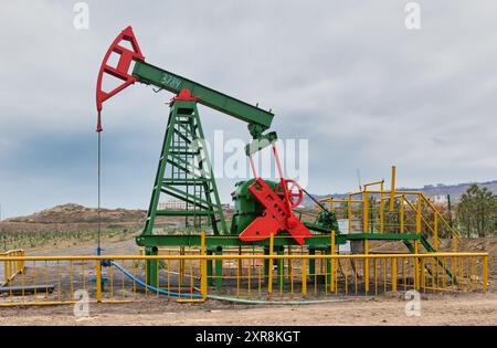 Ein funktionierender Ölpumpjack in grün und rot bemalt, umgeben von gelben Zäunen, vor einem bewölkten Himmel, in Baku, Aserbaidschan Stockfoto