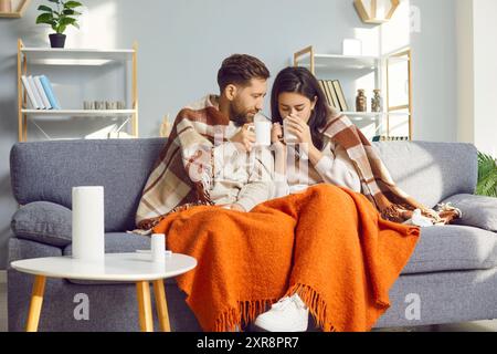 Ein junges Paar in Decken gewickelt, das zu Hause auf dem Sofa sitzt Stockfoto