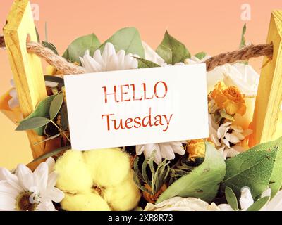 Die Worte "HELLO TUESDAY" auf einer weißen Visitenkarte, die auf einem Blumenstrauß platziert ist. Konzeptfoto Stockfoto