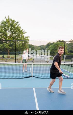 Frau und Mann spielen Pickleball auf dem Hof, lächelnd, genießen das Spiel Stockfoto