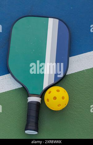 Pickleball-Paddel und gelber Ball auf dem grünen und blauen Platz. Stockfoto