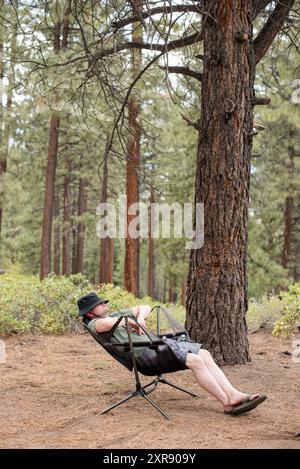 Ein Mann macht ein Nickerchen auf einem Campingstuhl im Wald Stockfoto