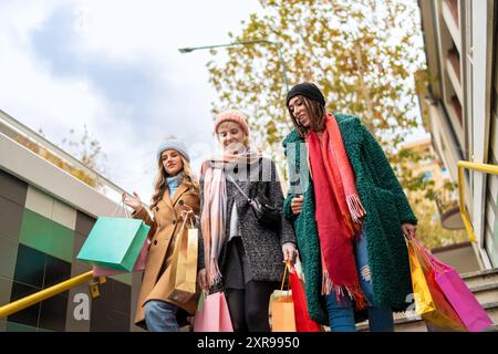 Drei stilvolle junge Frauen unterschiedlicher Ethnien auf einem Einkaufsbummel in der Stadt. Das Bild erfasst Freundschaft, Vielfalt und saisonale Modetrends a Stockfoto