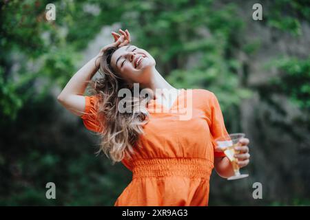 Junge Frau in orangefarbenem Kleid, die ein Picknick im Freien mit Champagner genießt Stockfoto