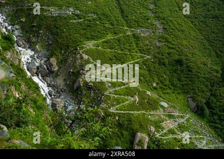Ein langer Zickzackpfad entlang eines Wasserfalls auf einem Bergkamm im höheren Himalaya von Himachal Pradesh, Indien. Die Pfadkomponenten Stockfoto