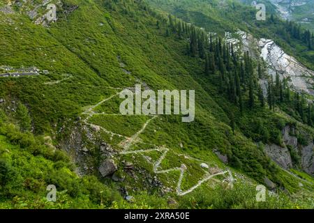 Ein langer Zickzackpfad entlang eines Wasserfalls auf einem Bergkamm im höheren Himalaya von Himachal Pradesh, Indien. Die Pfadkomponenten Stockfoto