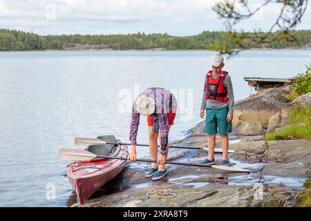 Vater und Sohn bereiten Kajak und Paddel für Kajaktouren am Meer, Kanu fahren, Bootstouren in der Ostsee während eines Familienurlaubs in Finnland vor. Stockfoto