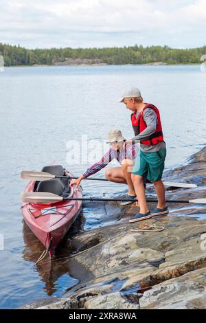 Vater und Sohn bereiten Kajak und Paddel für Kajaktouren am Meer, Kanu fahren, Bootstouren in der Ostsee während eines Familienurlaubs in Finnland vor. Stockfoto