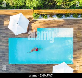 Mann schwimmt allein im Pool der Luxusvilla. Draufsicht aus der Luft. Bild des unvorsichtigen Sommerurlaubs Stockfoto