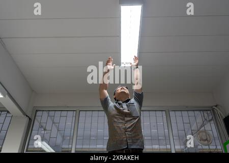 Energiesparende Glühlampe in einer weißen Deckenlampe, die Leuchtstofflampen in Gebäuden überprüft oder ersetzt. Glücklicher Mann, der ein l wechselt Stockfoto