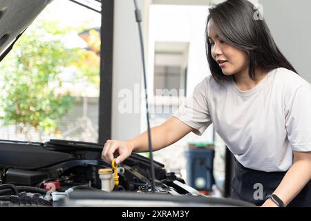 Asiatische Fahrerin überprüft Probleme mit dem Kühler, weibliche Kontrollen machen Fahrzeugmotor kaputt. Frau, die zu Hause den Ölstand im Automotor überprüft. Konzept von Stockfoto