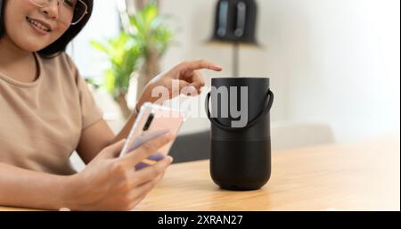 Frau streamt Musik oder Podcasts von einem Mobiltelefon zu Hause auf Smart Speaker. Nahaufnahme eines kabellosen Lautsprechers vor einer Frau, die auf einem Schreibtisch sitzt Stockfoto