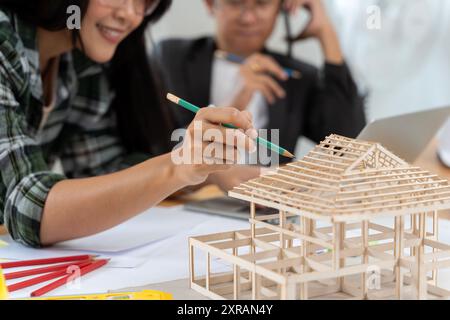 Architekten arbeiten an einem Hausmodell in einem kreativen Büro. Zwei junge Geschäftsleute diskutieren über ein neues Designprojekt, arbeiten an einem Archite Stockfoto