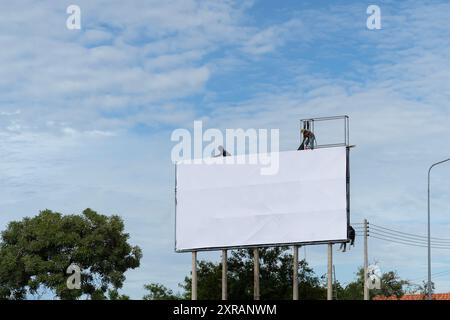 Mitarbeiter bereitet Reklametafeln auf die Installation neuer Werbung vor. Industrieklimpern arbeiten an einer Leiter - Platzieren eines Werbebanner. Arbeiter hängen eine Straße auf Stockfoto