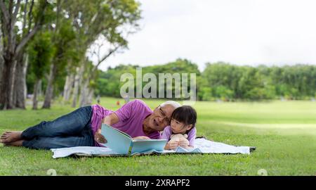 Glücklicher asiatischer Großvater und Enkelin im Park verbringen Freizeit mit Lesen im Freien. Ruhe, Entspannung, Bildung. Familienvergnügen auf dem Stockfoto