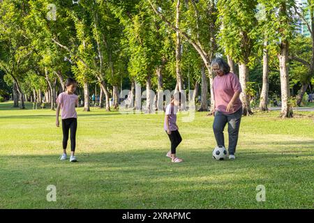 Gesunde und glückliche Großmutter, während ihre Enkelin im Park Fußball spielt. Vorstellung von Großeltern, die Zeit mit einem jungen Mädchen verbringen. Stockfoto