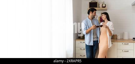 Romantisches junges Paar, das zusammen in der Küche kocht und eine gute Zeit zusammen hat. Lächelnder junger Mann, der Kaffeetasse hält, während die Freundin auf Ki sitzt Stockfoto
