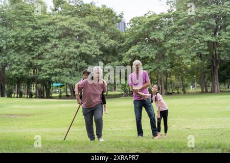 Seniorenpaar mit Enkelin auf einem Spaziergang draußen in der Natur. Senioren mit Enkelin, Sommertag. Menschen, die auf Gras laufen. Süße glückliche Kinder mit Stockfoto