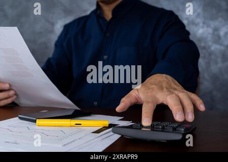 Ernsthafte und fokussierte Finanzbuchhaltung auf Papierarbeit im Büro. Geschäftsmann, der am Schreibtisch arbeitet, mit dem Rechner Zahlen, Berichte und Su berechnet Stockfoto