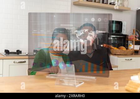 Glückliches Seniorenpaar, das einen Laptop benutzt, während er einen Urlaub zu Hause plant. Glückliches altes Paar, das sich mit dem Laptop unterhält und zusammen frühstückt, überrascht begeistert Stockfoto