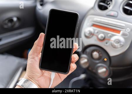 Junger Mann, der im Auto ein Smartphone benutzt. Nahansicht. Nahaufnahme Mann Hand hält Akku Mobiltelefon Smartphone im Auto aufladen. Modell leer b Stockfoto