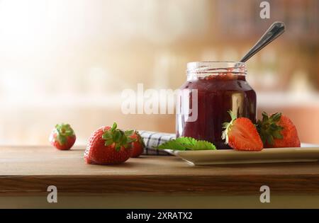 Glas mit Erdbeermarmelade auf weißem Teller mit Obst auf einem Holztisch und rustikalem Küchenhintergrund. Vorderansicht. Stockfoto