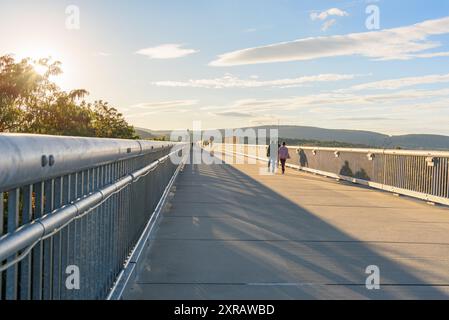 Menschen, die bei Sonnenuntergang im Herbst auf einer Fußgängerbrücke spazieren gehen Stockfoto