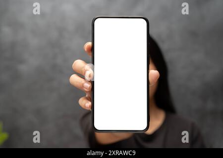 Eine schöne Frau, die mit dem Finger auf das Handy zeigt, mit einem leeren weißen Bildschirm. Nahaufnahme einer asiatischen Frau, die ein Mobiltelefon mit leerem Bildschirm zeigt Stockfoto