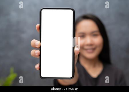 App-Anzeige. Lächelnde, hübsche Frau, die ein Smartphone mit weißem, leerem Geräteschild in der Hand hält, ganz in der Nähe der Kamera. Gadget mit freiem Platz für Mockup, BA Stockfoto