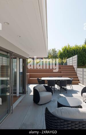 Außenbalkon der Villa modena mit einem kleinen Wohnzimmer bestehend aus einem Sofa, zwei Sesseln und einem Tisch mit Stühlen. Holztreppen führen zum Pool. Stockfoto