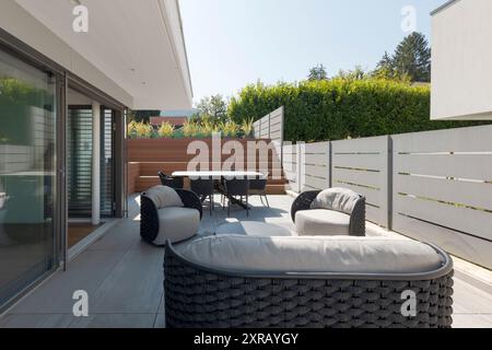 Außenbalkon der Villa modena mit einem kleinen Wohnzimmer bestehend aus einem Sofa, zwei Sesseln und einem Tisch mit Stühlen. Holztreppen führen zum Pool. Stockfoto